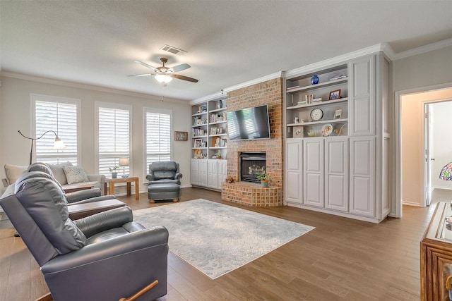 living area with crown molding, visible vents, a brick fireplace, ceiling fan, and wood finished floors