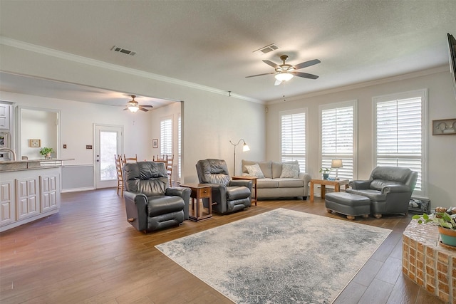 living room featuring a textured ceiling, dark wood-style flooring, visible vents, and crown molding