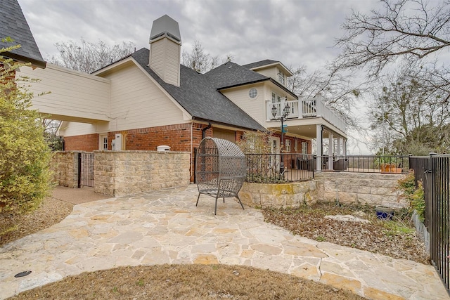 exterior space with roof with shingles, brick siding, a patio, fence, and a balcony