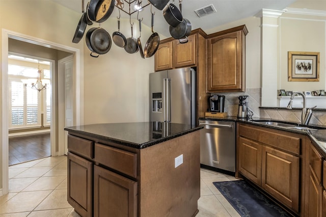 kitchen with light tile patterned floors, a sink, appliances with stainless steel finishes, a center island, and tasteful backsplash