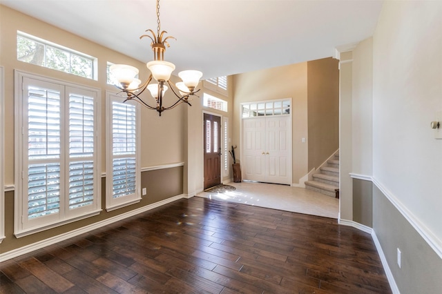 foyer entrance featuring baseboards, stairway, hardwood / wood-style flooring, and a notable chandelier