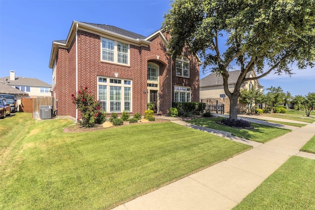 traditional-style home featuring a front yard, fence, cooling unit, and brick siding