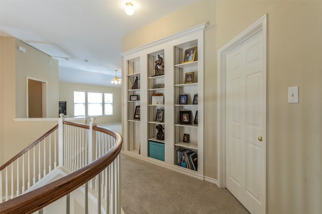 hall with built in shelves, carpet, an upstairs landing, and attic access