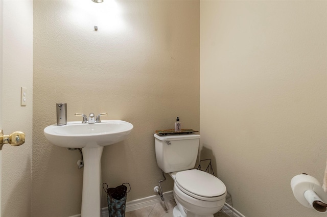 half bath with toilet, baseboards, and tile patterned floors