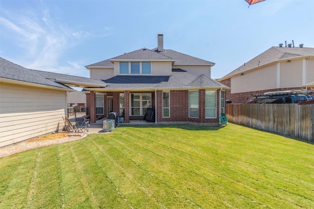 rear view of house featuring brick siding, fence, roof with shingles, a lawn, and a patio area