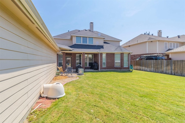 rear view of property featuring a patio, brick siding, a shingled roof, fence, and a yard