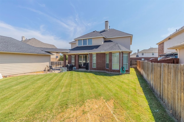 rear view of house featuring a lawn, a fenced backyard, a chimney, a patio area, and brick siding