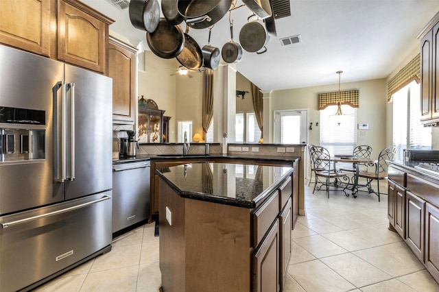 kitchen with a center island, light tile patterned floors, stainless steel appliances, visible vents, and dark stone counters