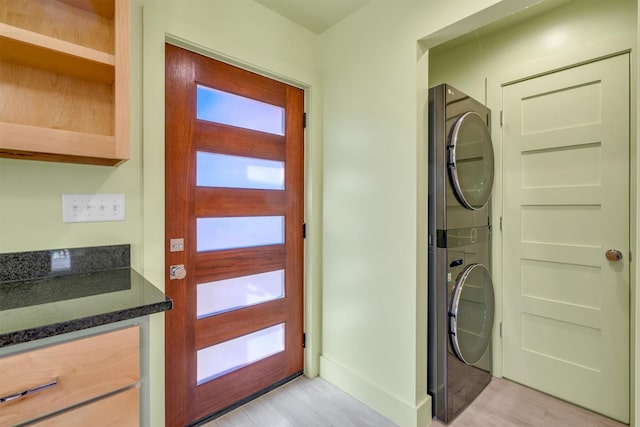 washroom with laundry area, light wood-style floors, baseboards, and stacked washing maching and dryer