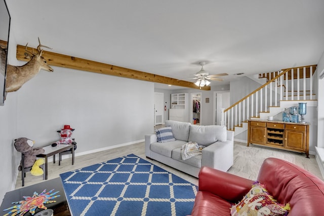 living area featuring baseboards, a ceiling fan, stairs, light wood-type flooring, and beam ceiling