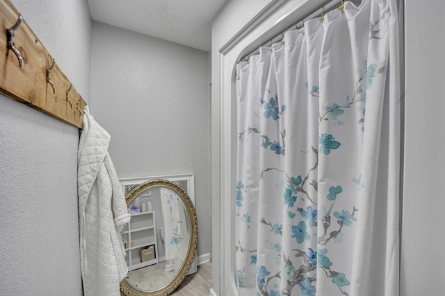 full bath featuring a shower with curtain, a textured wall, and wood finished floors