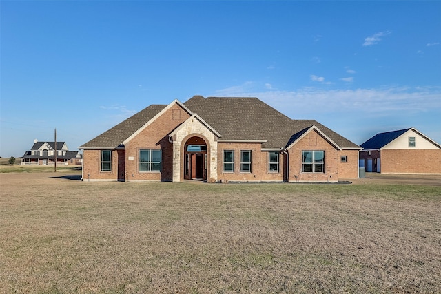 view of front facade with brick siding, roof with shingles, and a front yard