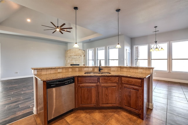 kitchen with a raised ceiling, stainless steel dishwasher, a sink, and light stone countertops