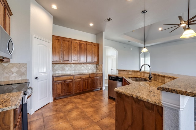 kitchen with arched walkways, brown cabinets, decorative backsplash, appliances with stainless steel finishes, and a sink