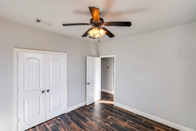 unfurnished bedroom with dark wood-style flooring, a closet, visible vents, a ceiling fan, and baseboards