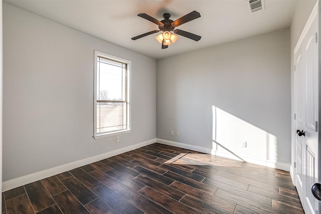 unfurnished room with ceiling fan, dark wood finished floors, visible vents, and baseboards