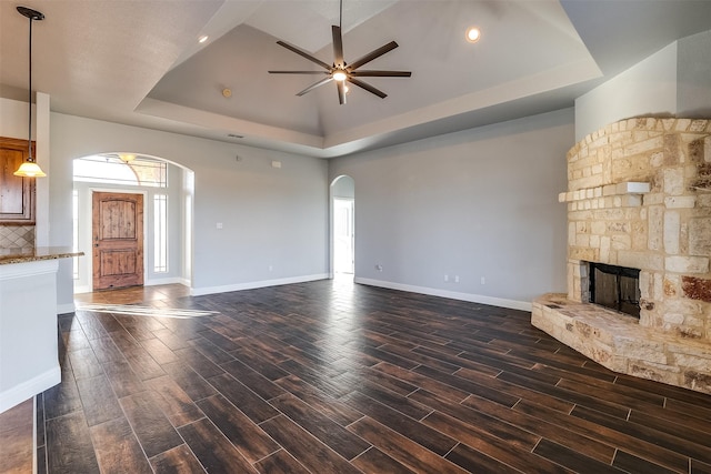 unfurnished living room with arched walkways, a tray ceiling, a fireplace, and wood tiled floor