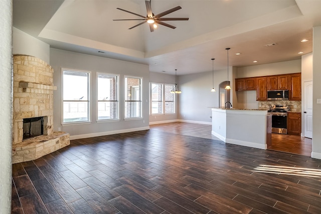 unfurnished living room featuring dark wood-style flooring, a fireplace, baseboards, and ceiling fan