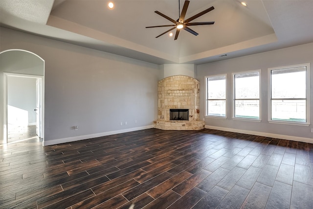 unfurnished living room with baseboards, a stone fireplace, a raised ceiling, and wood tiled floor