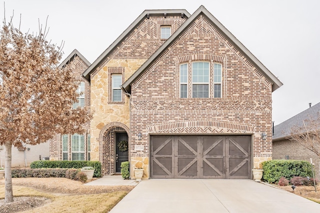 french country style house featuring an attached garage, stone siding, brick siding, and concrete driveway