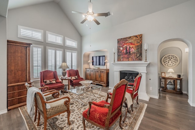 living room featuring baseboards, high vaulted ceiling, a fireplace with raised hearth, and wood finished floors