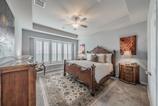 carpeted bedroom with visible vents, a tray ceiling, ceiling fan, and baseboards