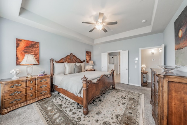 bedroom with a tray ceiling, light carpet, ceiling fan, and baseboards