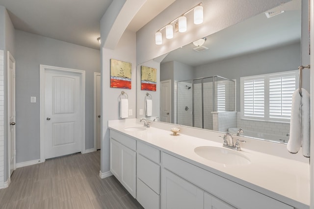 bathroom with double vanity, a stall shower, baseboards, and a sink