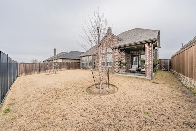 back of house featuring brick siding, a patio, a chimney, a shingled roof, and a fenced backyard