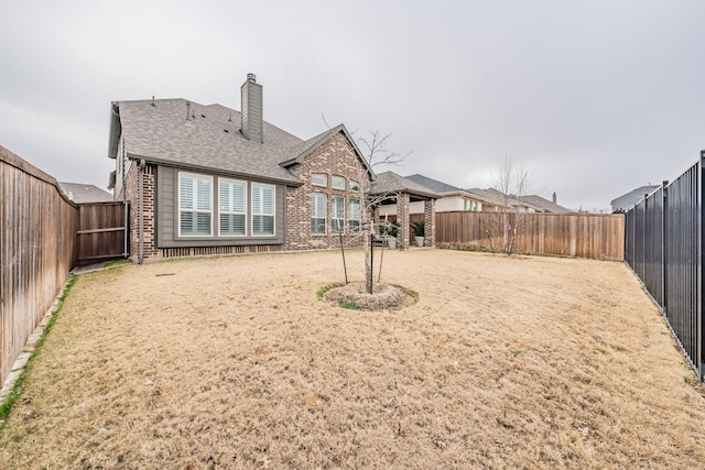 back of property featuring brick siding, a chimney, a shingled roof, and a fenced backyard