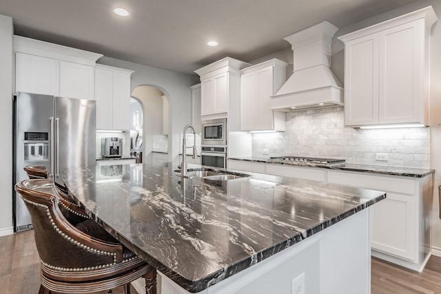 kitchen featuring a spacious island, custom range hood, decorative backsplash, appliances with stainless steel finishes, and light wood-type flooring