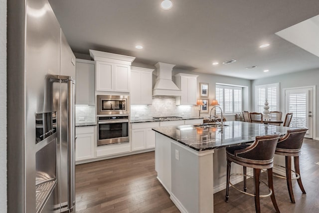 kitchen with a kitchen breakfast bar, a sink, custom exhaust hood, stainless steel appliances, and backsplash