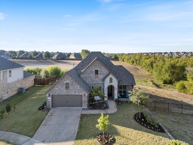 french provincial home with central AC, fence, stone siding, driveway, and a front lawn