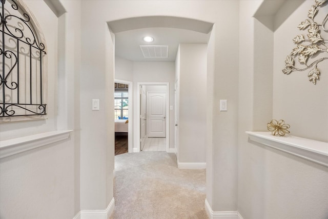 hall with arched walkways, light colored carpet, visible vents, and baseboards