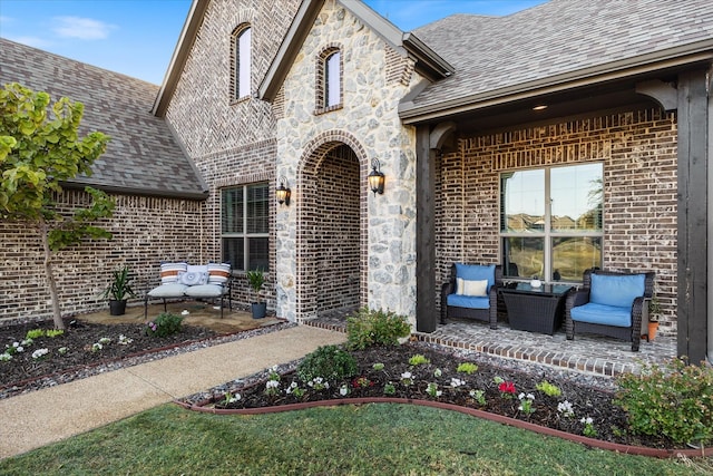 property entrance with stone siding, roof with shingles, a patio area, and brick siding