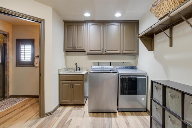 clothes washing area with a sink, baseboards, light wood-type flooring, cabinet space, and washing machine and clothes dryer