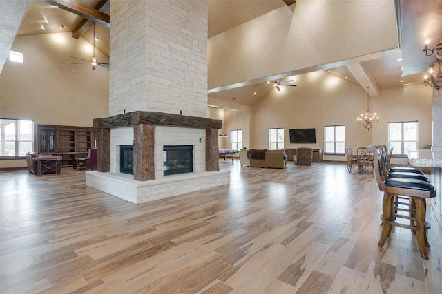 unfurnished living room featuring wood finished floors, beamed ceiling, a fireplace, high vaulted ceiling, and ceiling fan with notable chandelier