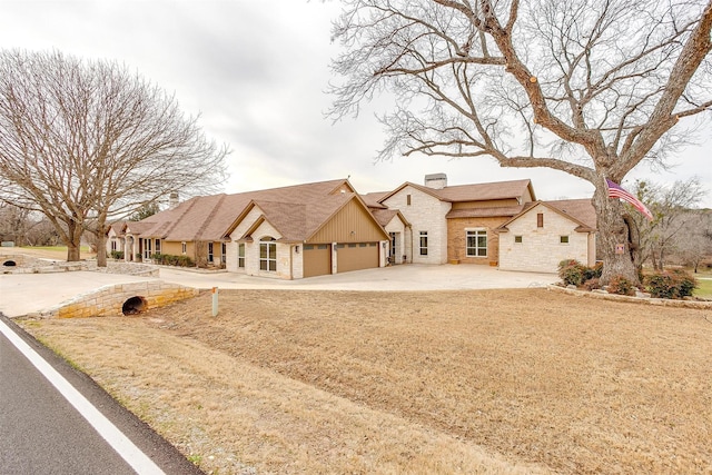 view of front of property featuring stone siding, a chimney, an attached garage, and concrete driveway