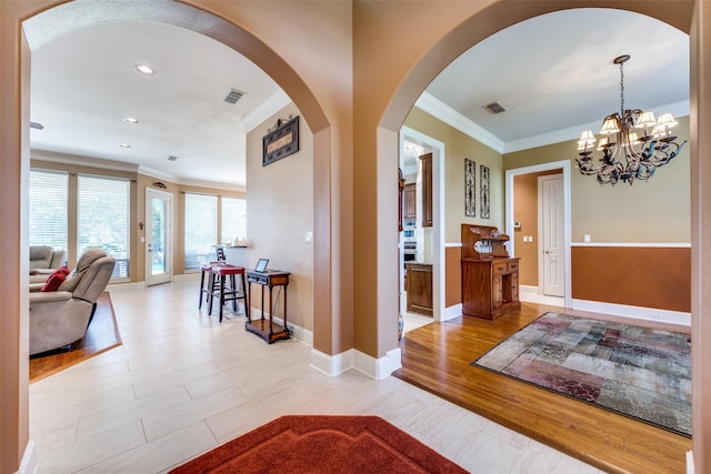 foyer featuring ornamental molding, arched walkways, visible vents, and light wood-style floors