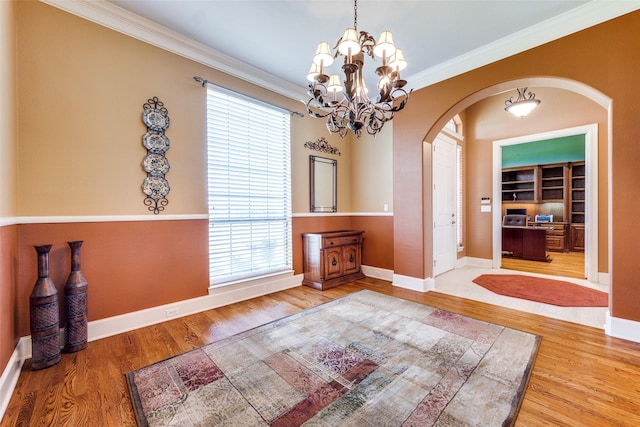 unfurnished dining area featuring arched walkways, baseboards, wood finished floors, and crown molding