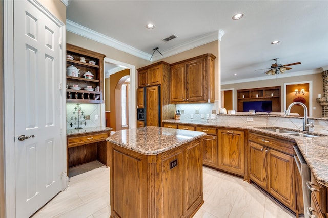 kitchen with arched walkways, a center island, brown cabinets, visible vents, and a sink