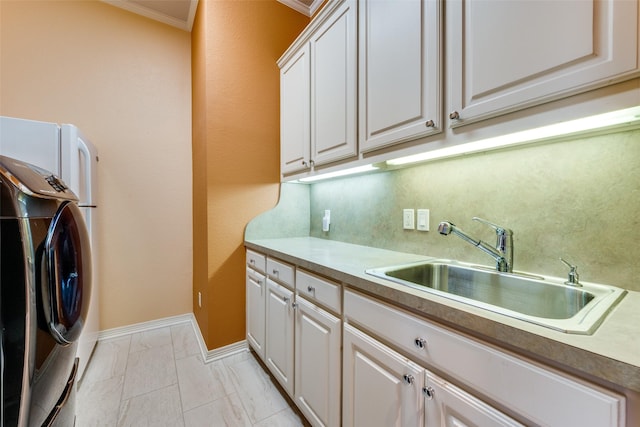 washroom with cabinet space, ornamental molding, washing machine and dryer, a sink, and baseboards