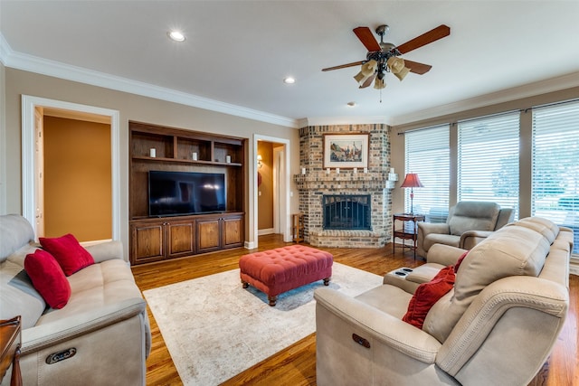 living room with crown molding, a fireplace, a ceiling fan, and wood finished floors