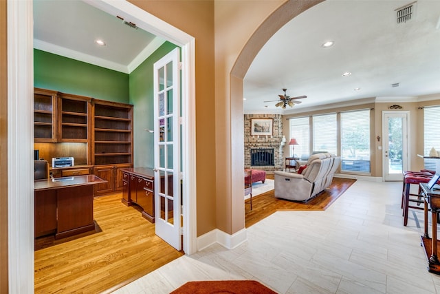 interior space with arched walkways, crown molding, a fireplace, ceiling fan, and baseboards