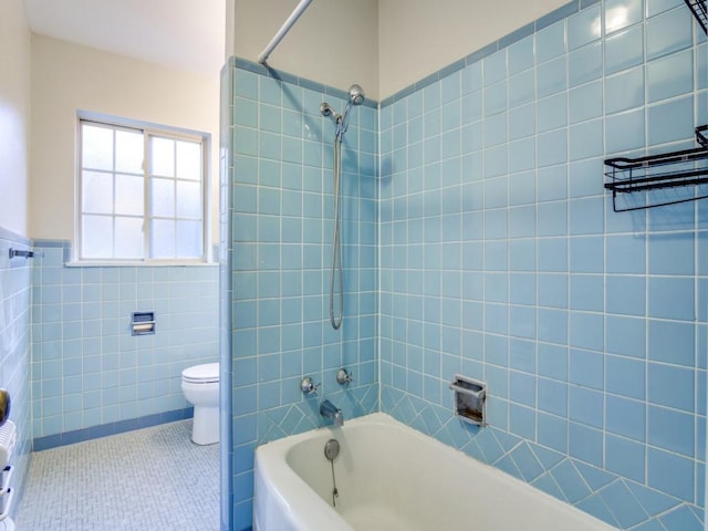 bathroom featuring tile walls, bathtub / shower combination, toilet, wainscoting, and tile patterned floors