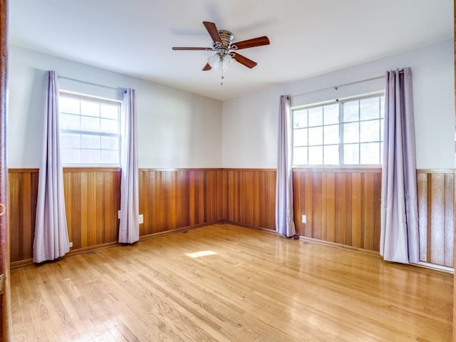 spare room featuring a wainscoted wall, plenty of natural light, wooden walls, and wood finished floors