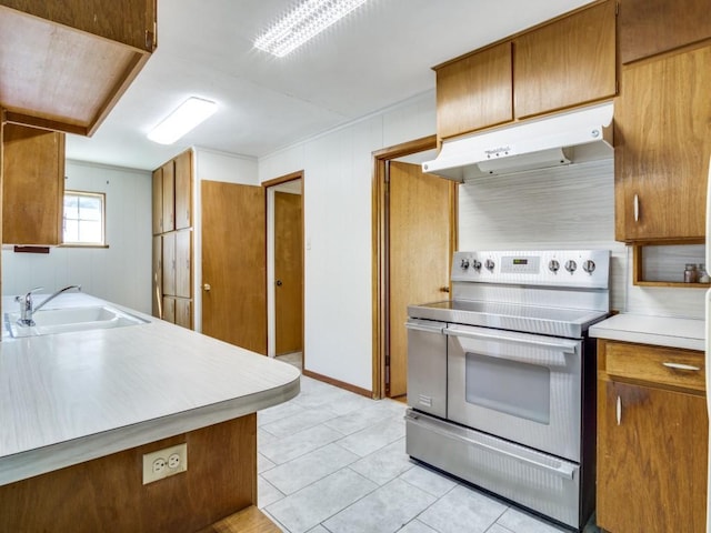 kitchen featuring light countertops, brown cabinetry, stainless steel range with electric cooktop, a sink, and under cabinet range hood