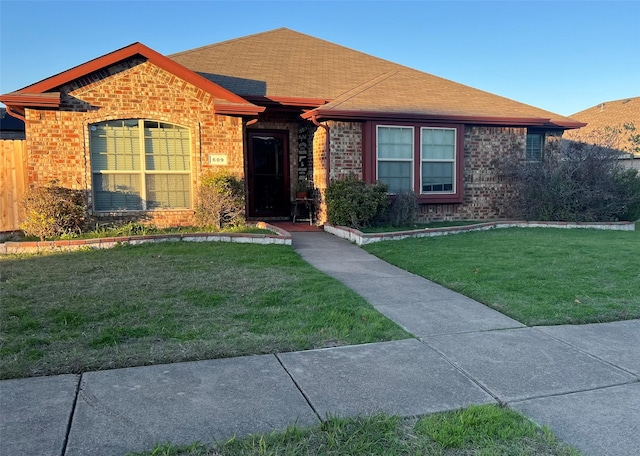 ranch-style home featuring brick siding, roof with shingles, a front yard, and fence