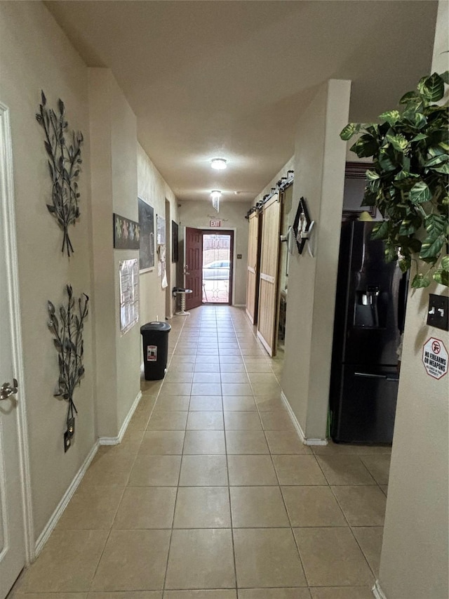 corridor featuring light tile patterned flooring, baseboards, and a barn door