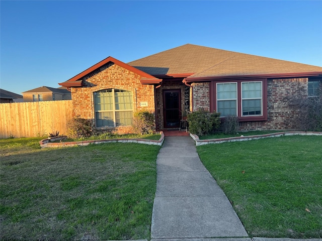 ranch-style house with brick siding, a shingled roof, fence, and a front yard